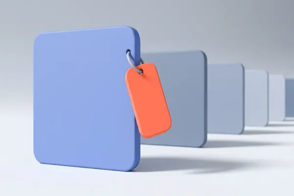 Una placa azul en primer plano con una etiqueta coral colgada de una anilla, y detrás una hilera de placas grisáceas iguales que se aleja, ninguna con etiqueta.